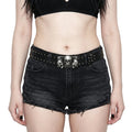Person wearing black denim shorts with a skull belt buckle on a plain background
