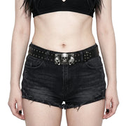 Person wearing black denim shorts with a skull belt buckle on a plain background