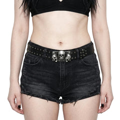 Person wearing black denim shorts with a skull belt buckle on a plain background